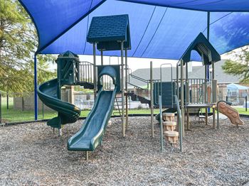 a playground with slides and other playground equipment under a blue tent at The Madison of Tyler Apartment Homes in Tyler, TX